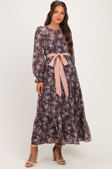 woman wearing a dark floral maternity dress with long sleeves and a pink ribbon belt, showcasing a baby bump