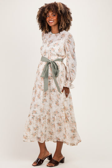 woman wearing a floral long sleeve maternity dress with a green belt and a flowing skirt