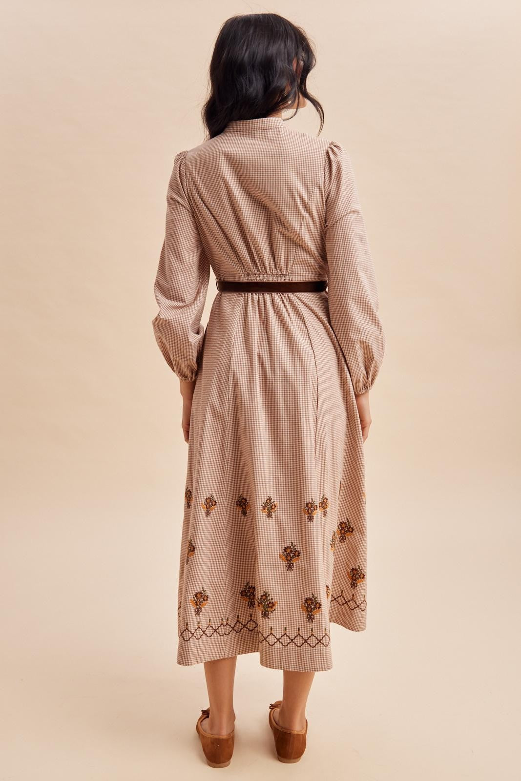 woman wearing a beige striped midi dress with floral embroidery at the hem and a brown belt, seen from the back