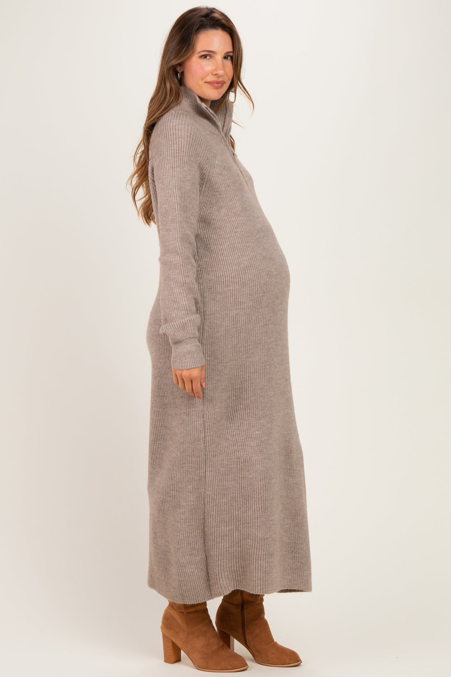 woman wearing a beige ribbed maternity sweater dress and showcasing her baby bump, paired with brown ankle boots