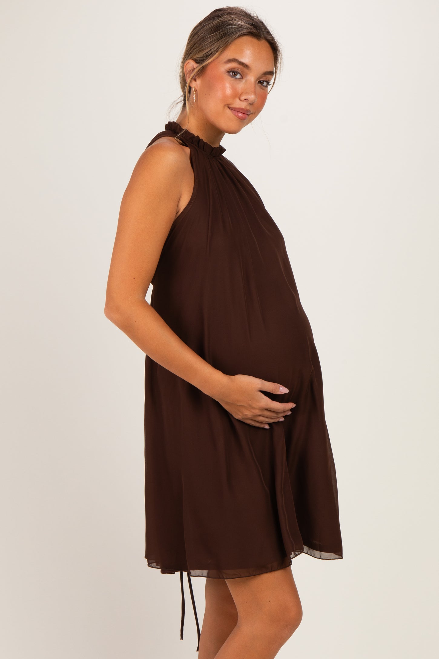 woman wearing a brown sleeveless maternity dress with a tie detail and showing her baby bump