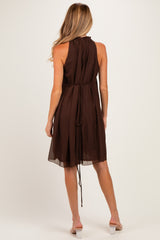 woman wearing a chocolate brown sleeveless maternity dress with a tied back detail and a flowing silhouette
