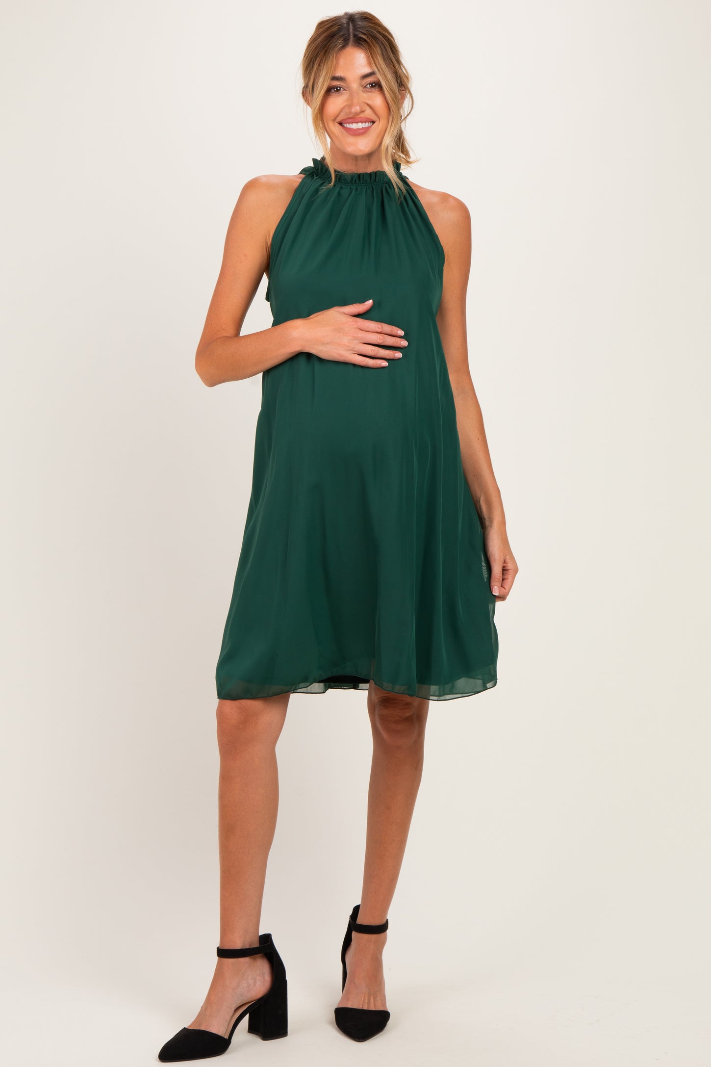 woman wearing a dark green halter neck maternity dress and holding her baby bump