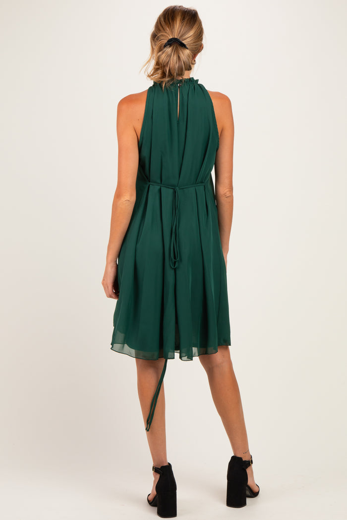 woman wearing a green maternity dress with a halter neck and a flowing skirt, showing a tied detail at the back