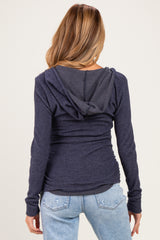woman wearing a navy blue maternity hoodie with a hood and gathered sides, showing a hint of a baby bump