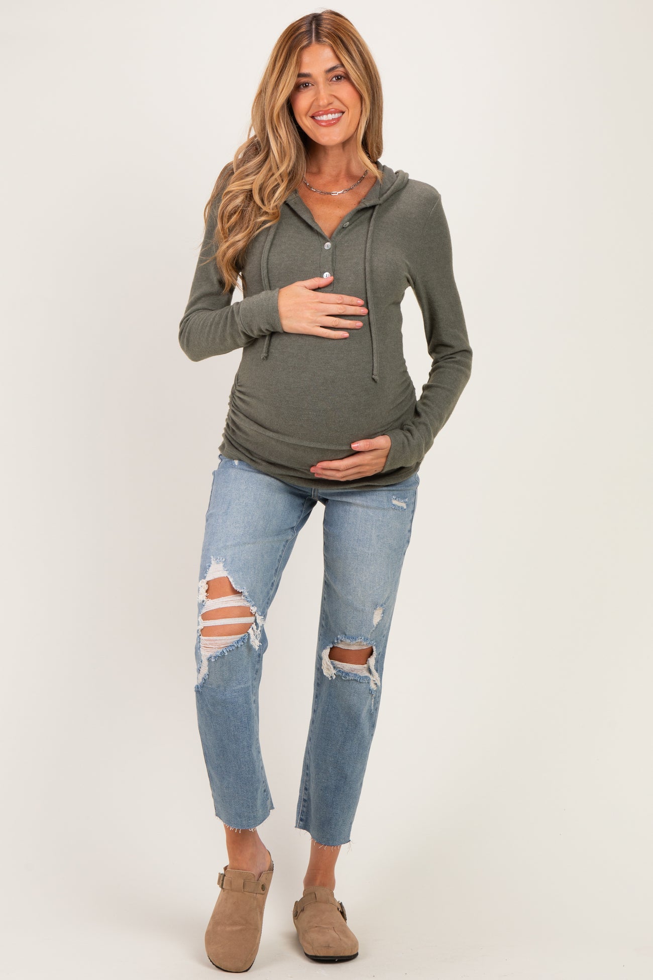 woman wearing a green maternity hoodie and distressed jeans, holding her baby bump