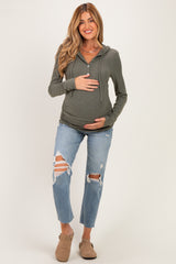 woman wearing a green maternity hoodie and distressed jeans, holding her baby bump