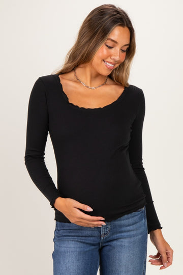 woman wearing a black long sleeve maternity top with a scalloped neckline and holding her baby bump
