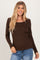 woman wearing a brown long sleeve top with a square neck and scalloped hem, smiling at the camera