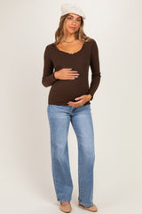 woman wearing a brown long sleeve maternity top with a scalloped neckline and blue flared jeans, holding her baby bump