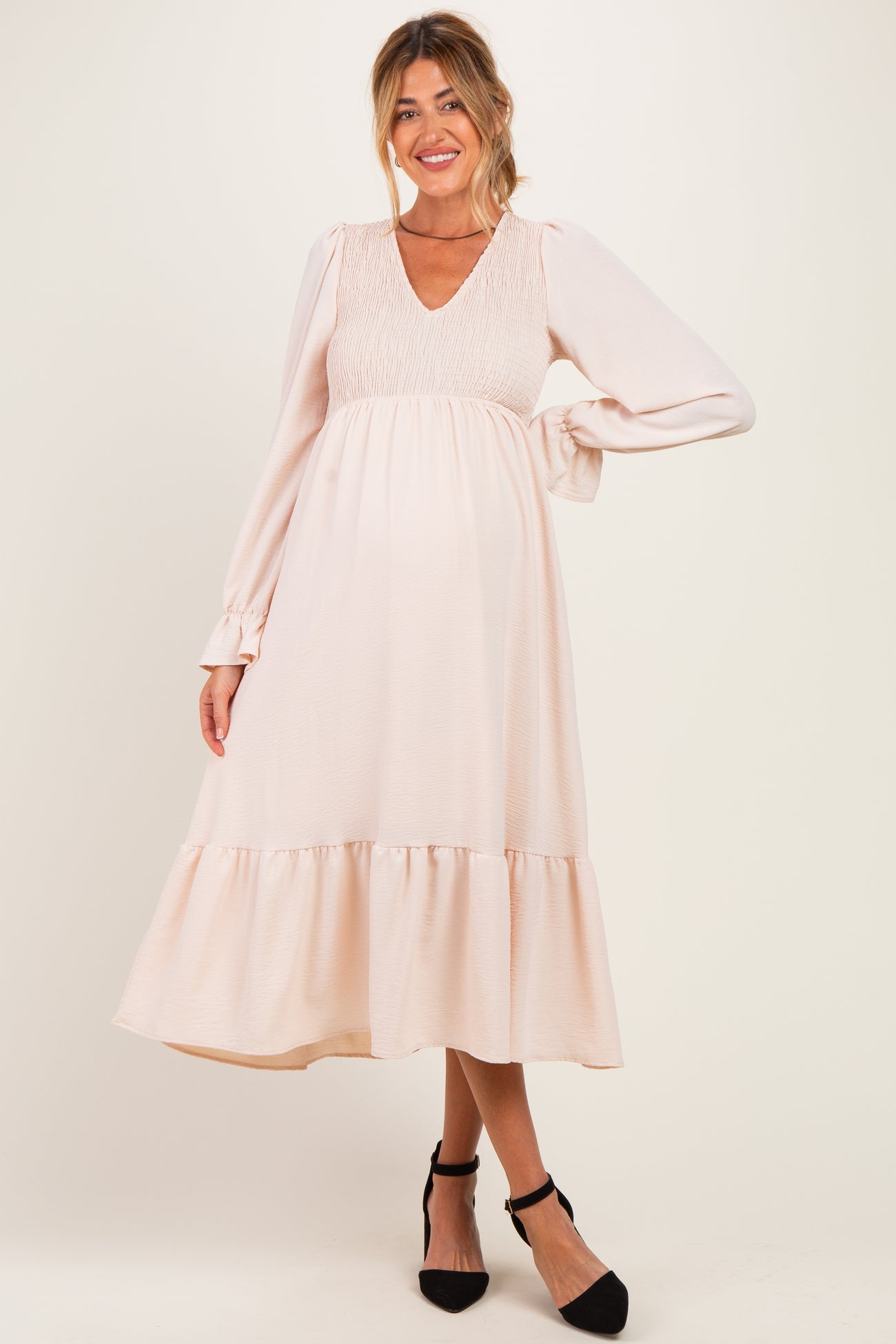 woman wearing a light pink maternity dress with a smocked bodice and long sleeves, holding her baby bump