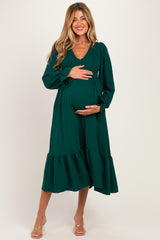 woman wearing a green maternity dress with long sleeves and a ruffled hem, holding her baby bump