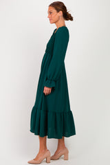 woman wearing a dark green long sleeve maxi dress with smocked bodice and ruffled hem, styled with nude heels