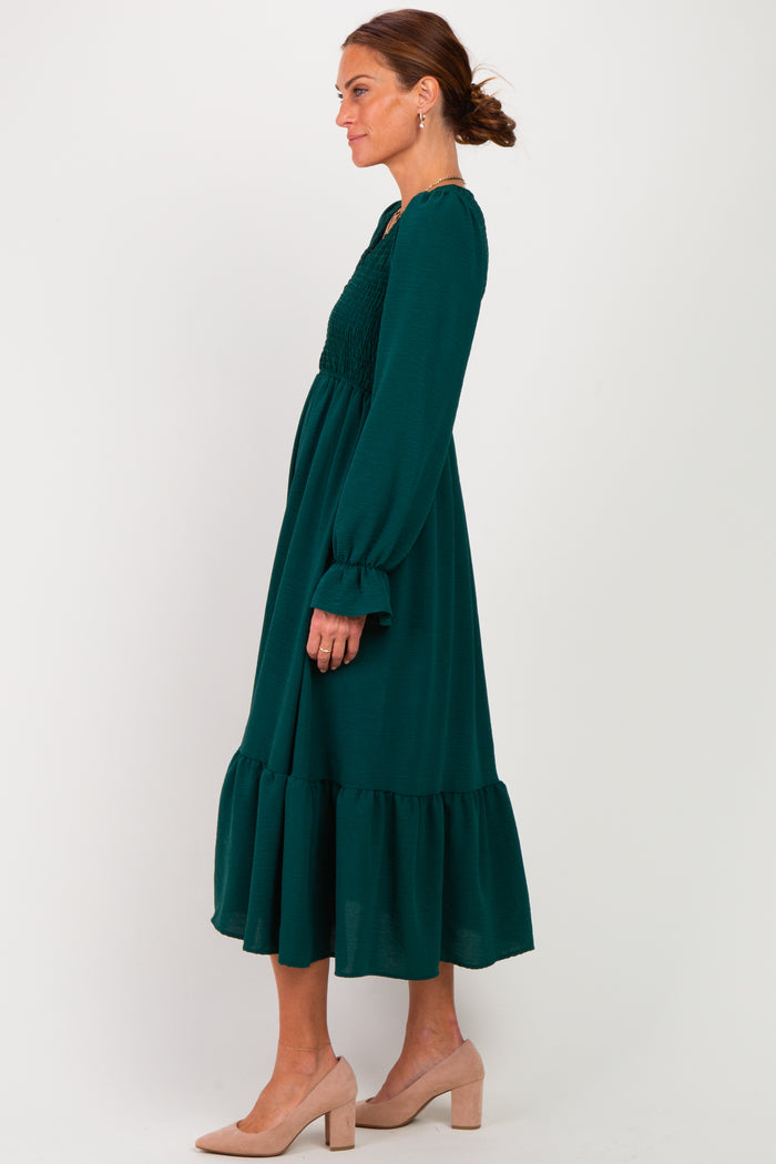 woman wearing a dark green long sleeve maxi dress with smocked bodice and ruffled hem, styled with nude heels