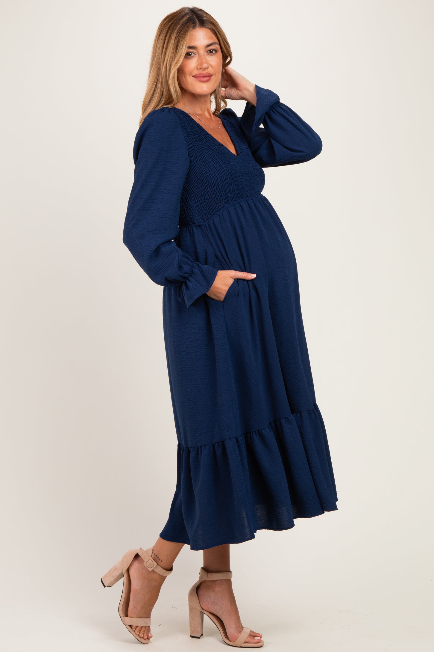 woman wearing a navy blue maternity dress with long sleeves, smocked bodice, and tiered skirt, showcasing her baby bump