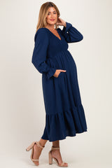 woman wearing a navy blue maternity dress with long sleeves, smocked bodice, and tiered skirt, showcasing her baby bump