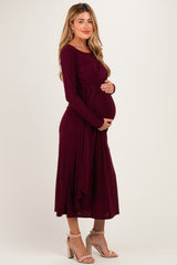 woman wearing a burgundy long sleeve maternity dress and holding her baby bump