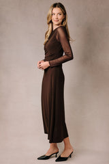 woman wearing a brown long sleeve dress with a fitted bodice and flowing skirt, paired with black heels