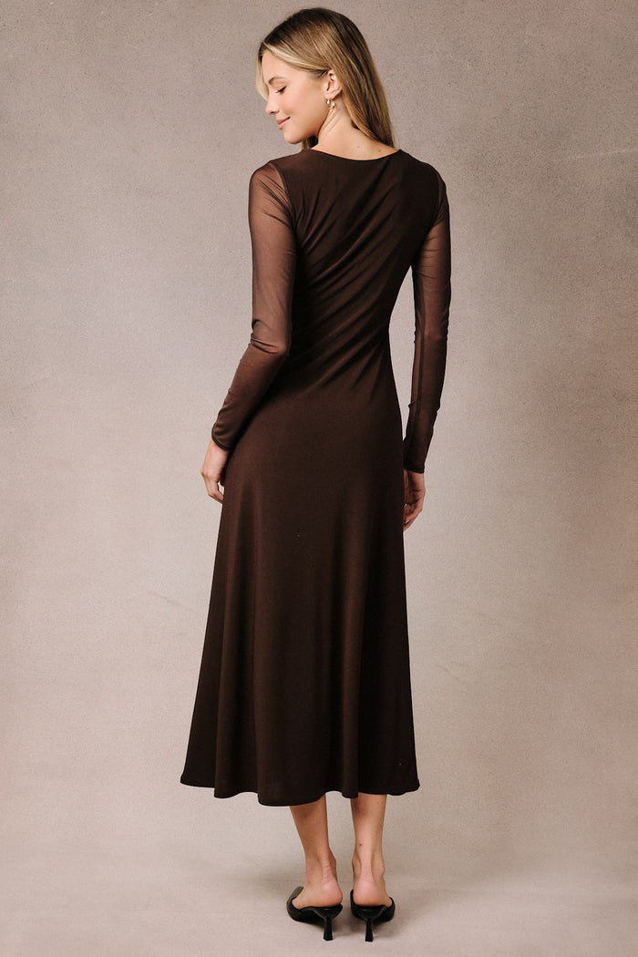 woman wearing a brown long sleeve dress with sheer sleeves and a flowy skirt, seen from the back