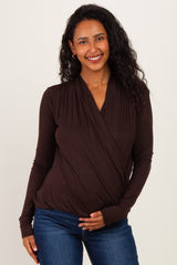 woman wearing a dark brown long sleeve maternity top and gently holding her baby bump