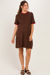 woman wearing a brown maternity dress with a red ruffled collar and sleeves, standing and showing her baby bump