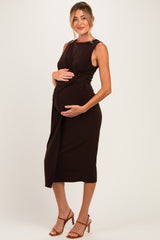 woman wearing a brown sleeveless maternity dress with a twisted waist and holding her baby bump