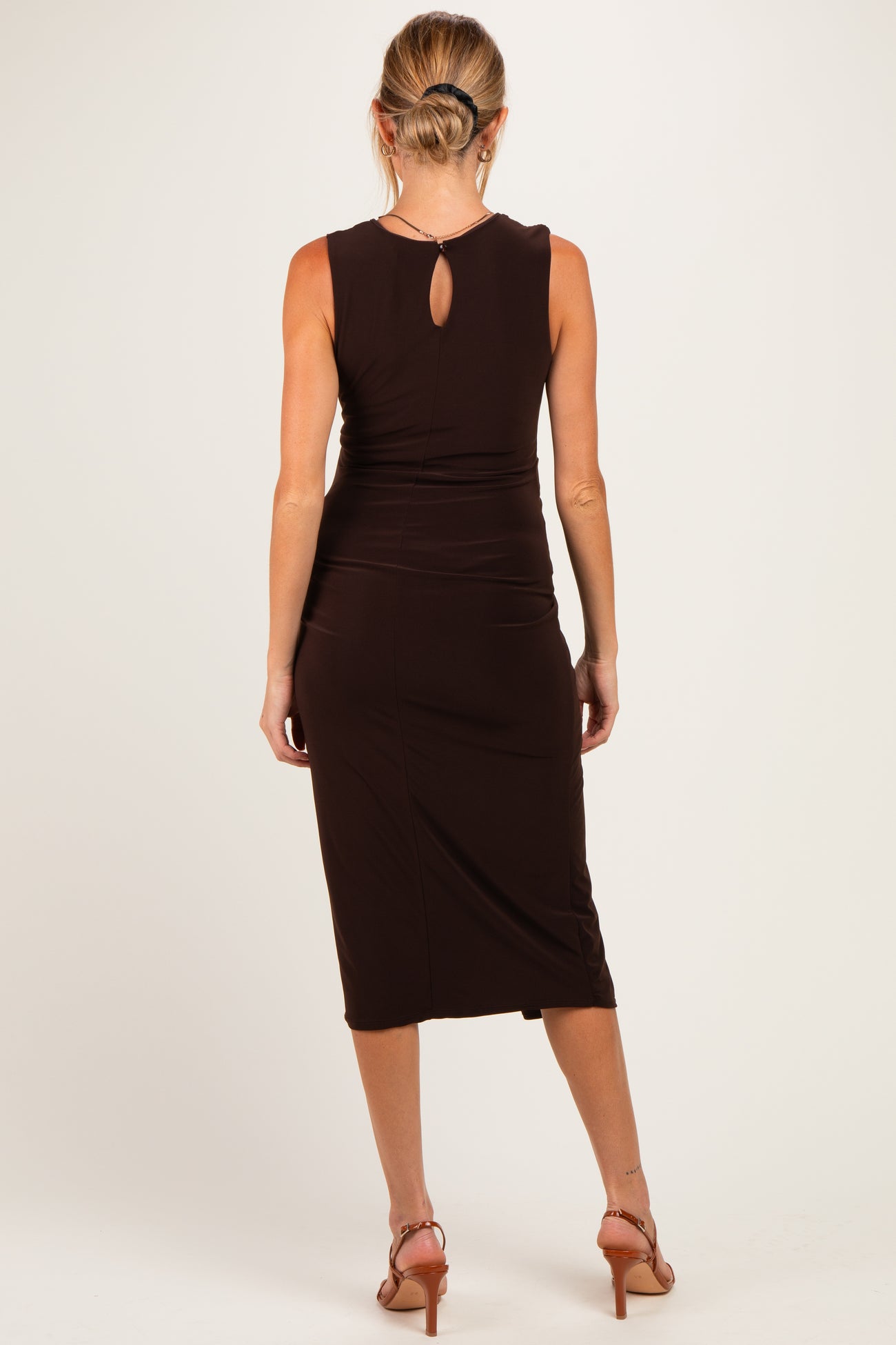 woman wearing a dark brown maternity dress with a keyhole back detail, mid-length and fitted silhouette