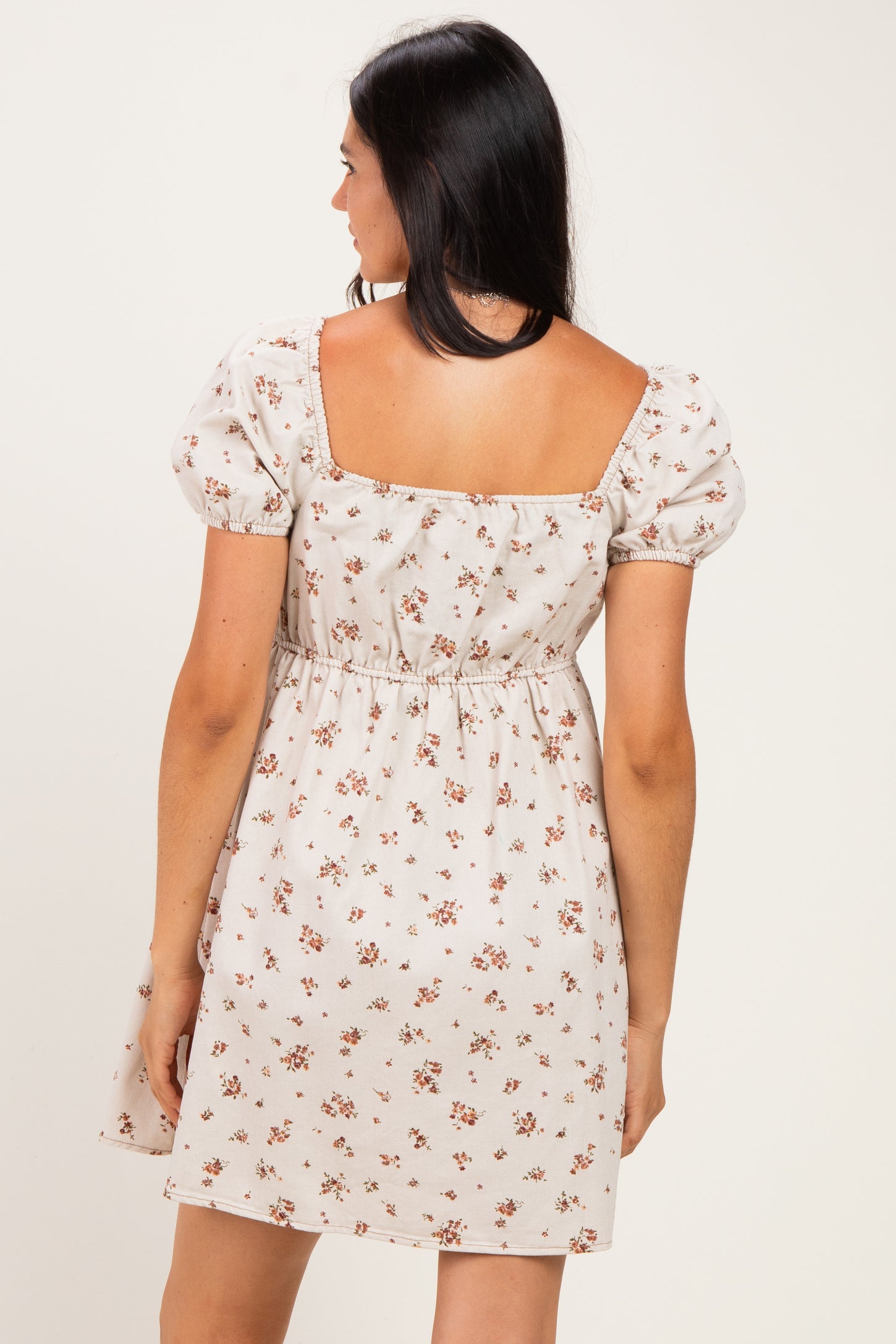 woman wearing a light beige floral short dress with puff sleeves and a fitted waist, shown from the back
