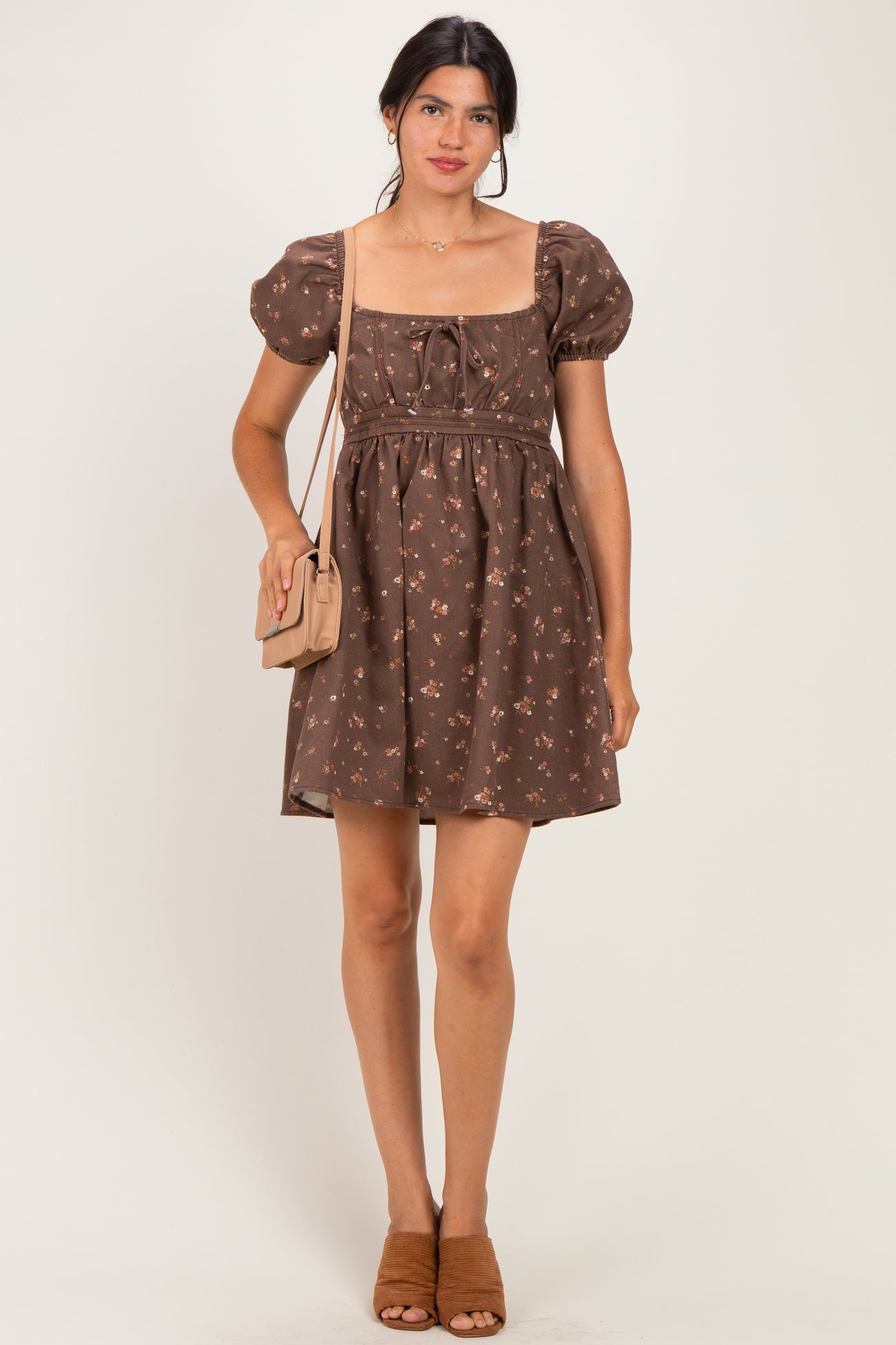 woman wearing a brown floral puff sleeve mini dress and holding a small handbag with a quilted design