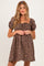 woman wearing a brown floral maternity dress with puff sleeves and a tie detail at the chest