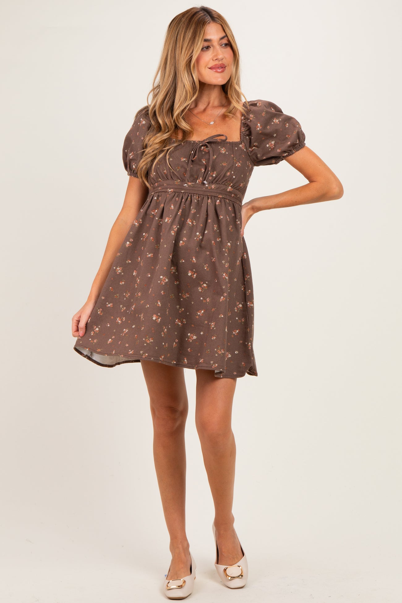 woman wearing a brown floral print maternity dress with puff sleeves and a tied neckline, showing off her baby bump