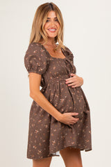 woman wearing a brown floral maternity dress with puff sleeves and a tie detail, cradling her baby bump