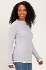 woman wearing a light gray ribbed long sleeve top with ruffled cuffs and hemline