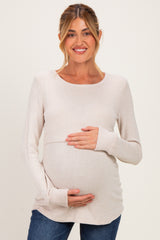 woman wearing a light beige long sleeve maternity top and holding her baby bump