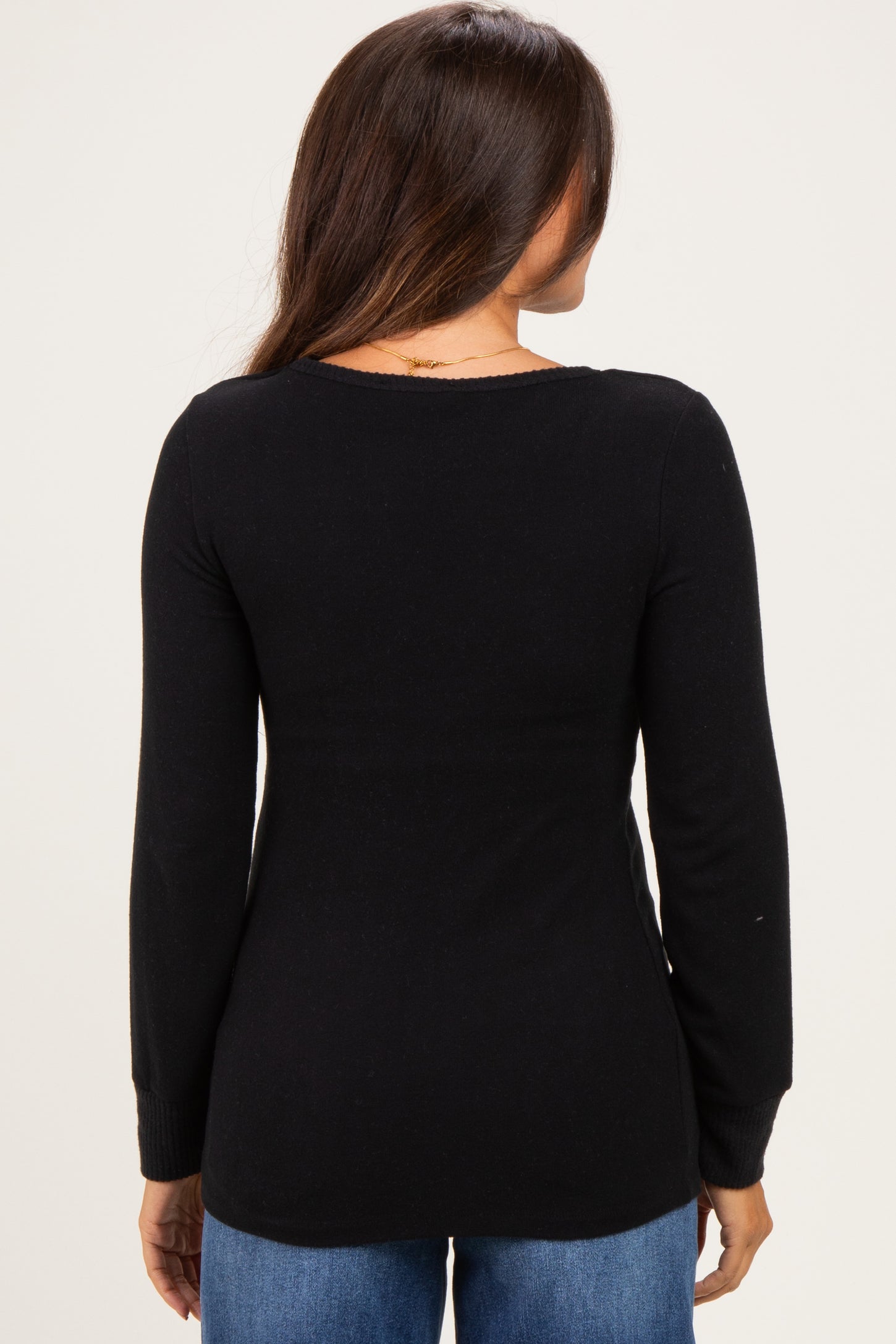 woman wearing a black long sleeve maternity top, viewed from the back, paired with blue jeans