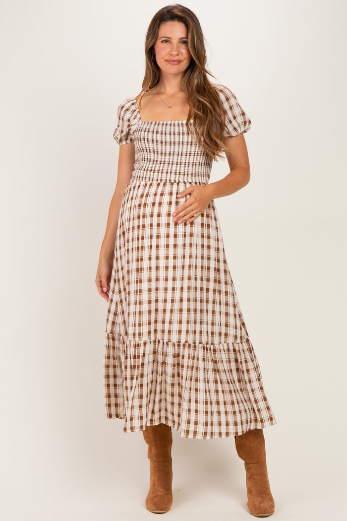 woman wearing a brown and white checkered midi maternity dress and holding her baby bump