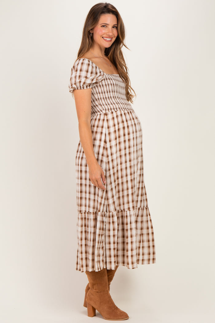 woman wearing a brown and white checked maternity dress with a smocked bodice and tiered skirt, showing her baby bump