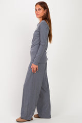 woman wearing a grey long sleeve top and wide-leg pants, standing sideways with a relaxed pose