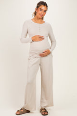 woman wearing a light beige maternity loungewear set with long sleeves and wide leg pants, holding her baby bump
