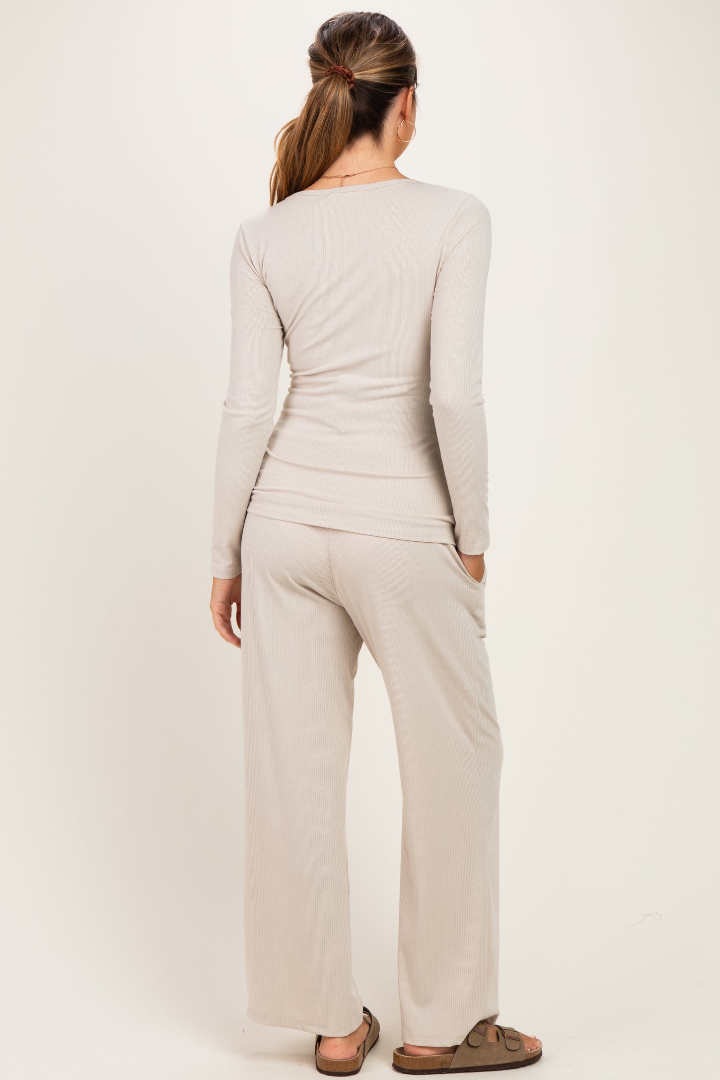 woman wearing a light beige long sleeve top and matching wide-leg pants, showing back view, styled for maternity wear