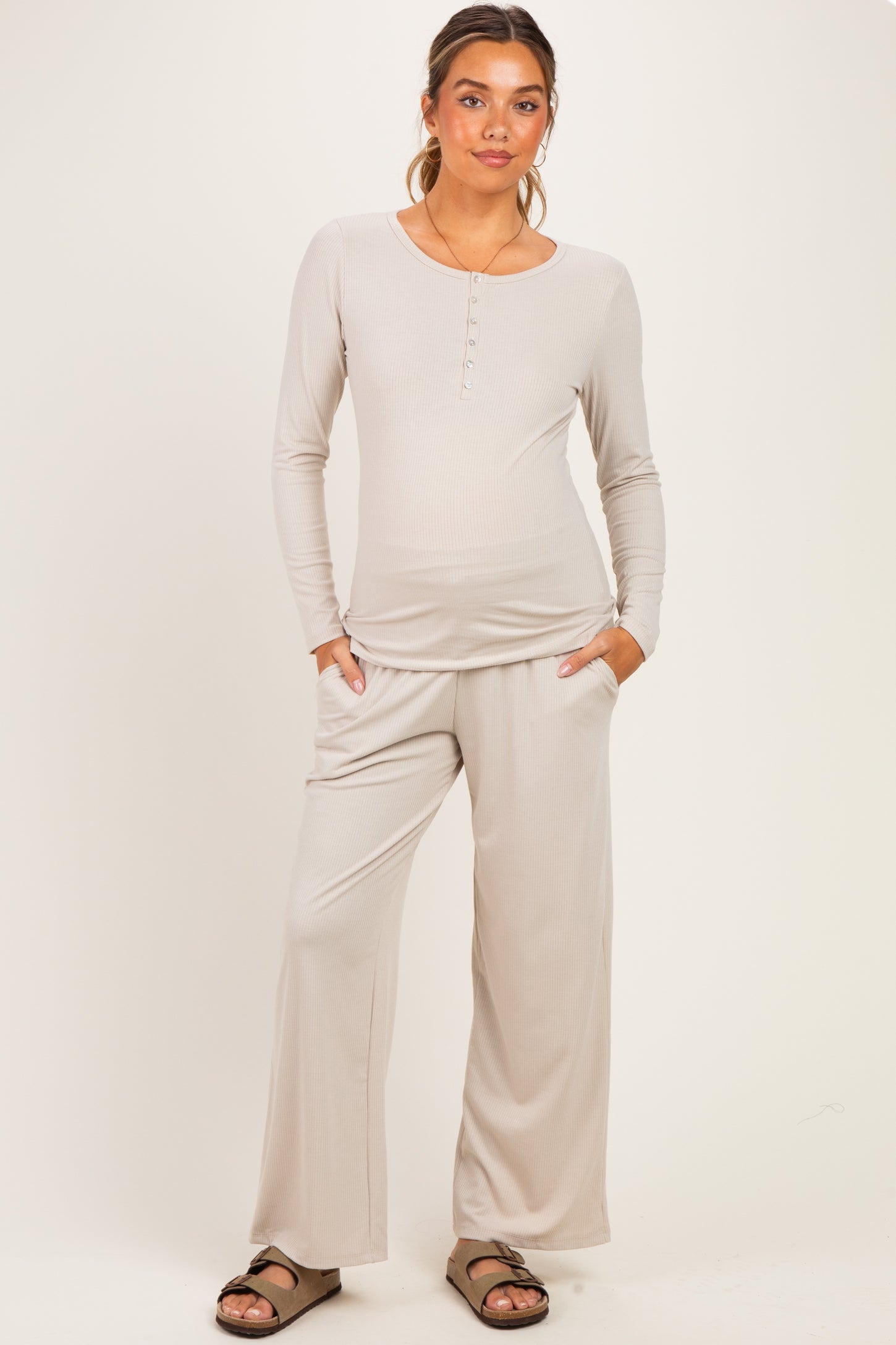 woman wearing a light taupe maternity loungewear set with a long sleeve henley top and wide-leg pants, baby bump visible