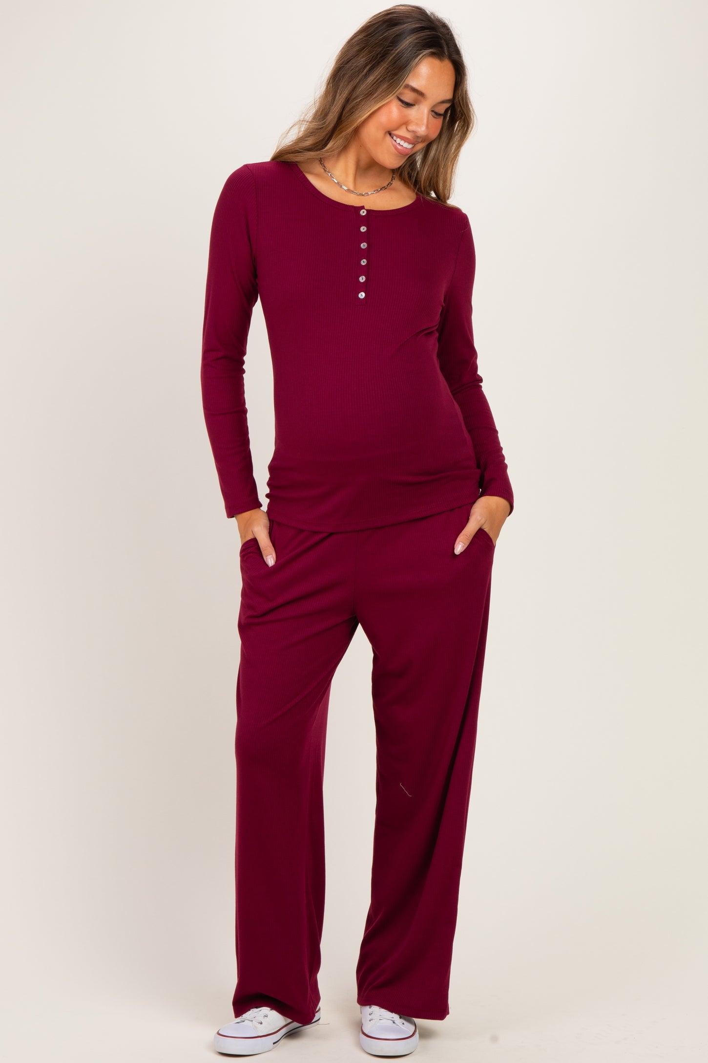 woman wearing a burgundy long sleeve maternity top with buttons and matching wide-leg maternity pants, showing her baby bump