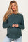 woman wearing a dark teal maternity sweater with long sleeves and a maternity-friendly fit, holding her baby bump