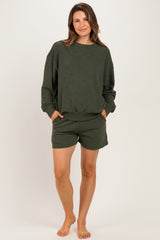 woman wearing a dark green maternity sweatshirt and matching shorts, pockets visible, comfortable casual style
