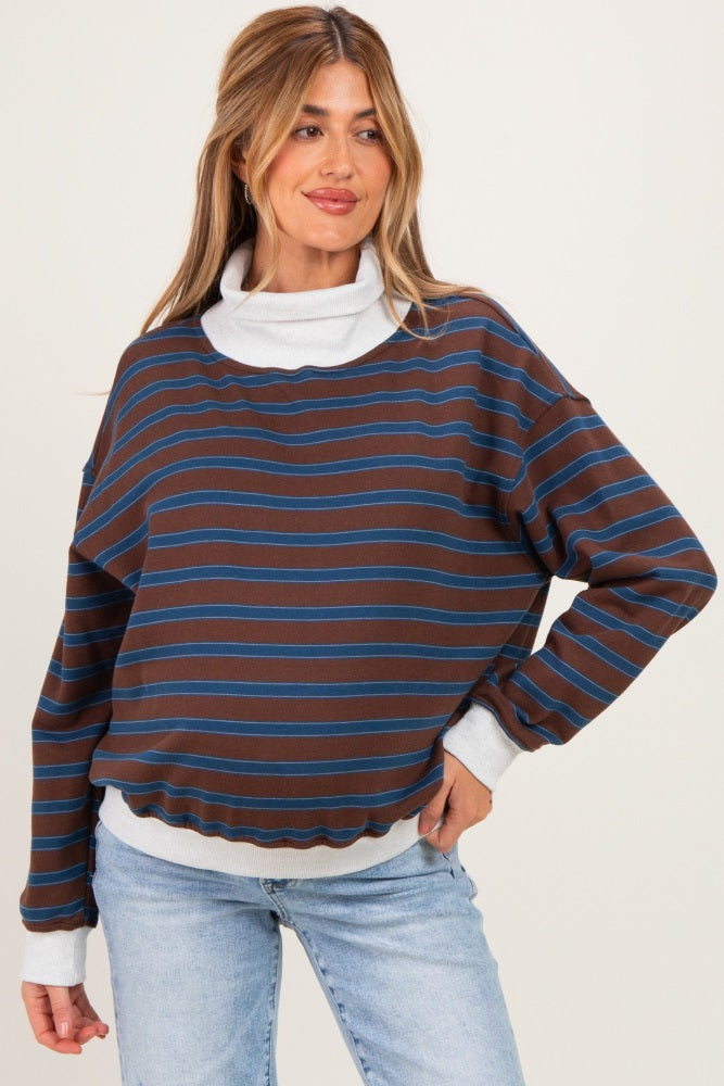woman wearing a brown striped maternity sweatshirt with a white turtleneck underneath, styled with blue jeans