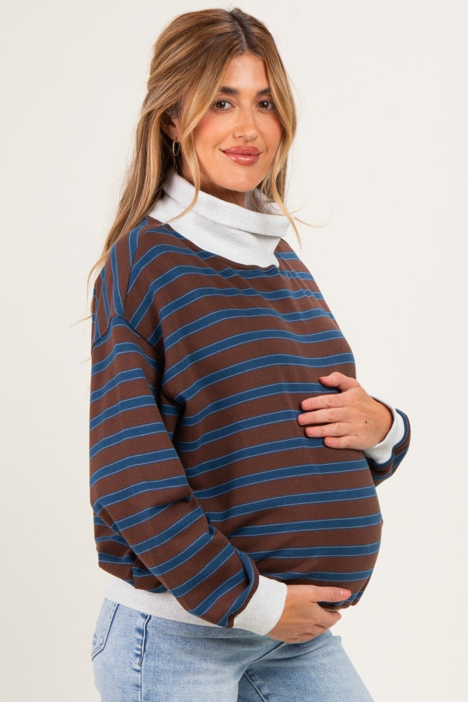 woman wearing a brown and blue striped maternity sweatshirt with a cowl neck and holding her baby bump