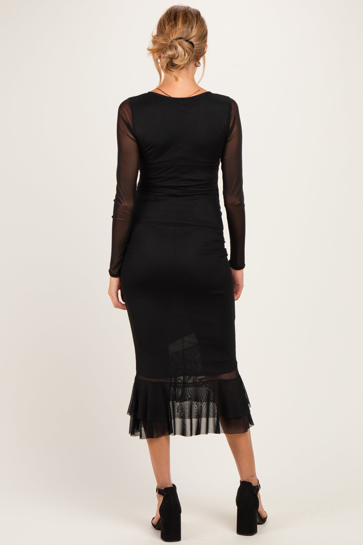 woman wearing a black long sleeve maternity dress with a flared sheer hem and fitted silhouette, showing a baby bump