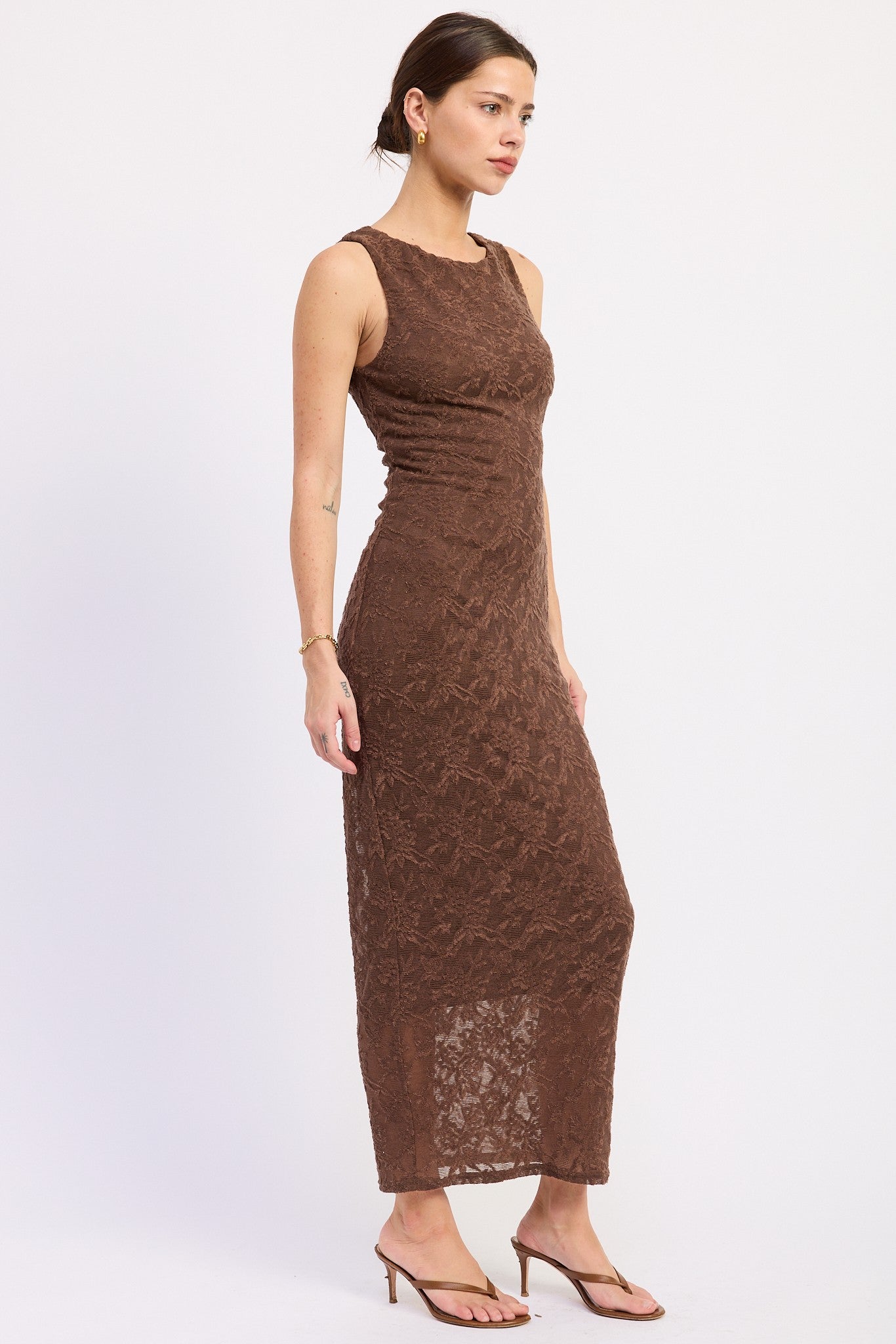 woman wearing a brown lace maxi dress with a fitted bodice and a long skirt, paired with strappy heels