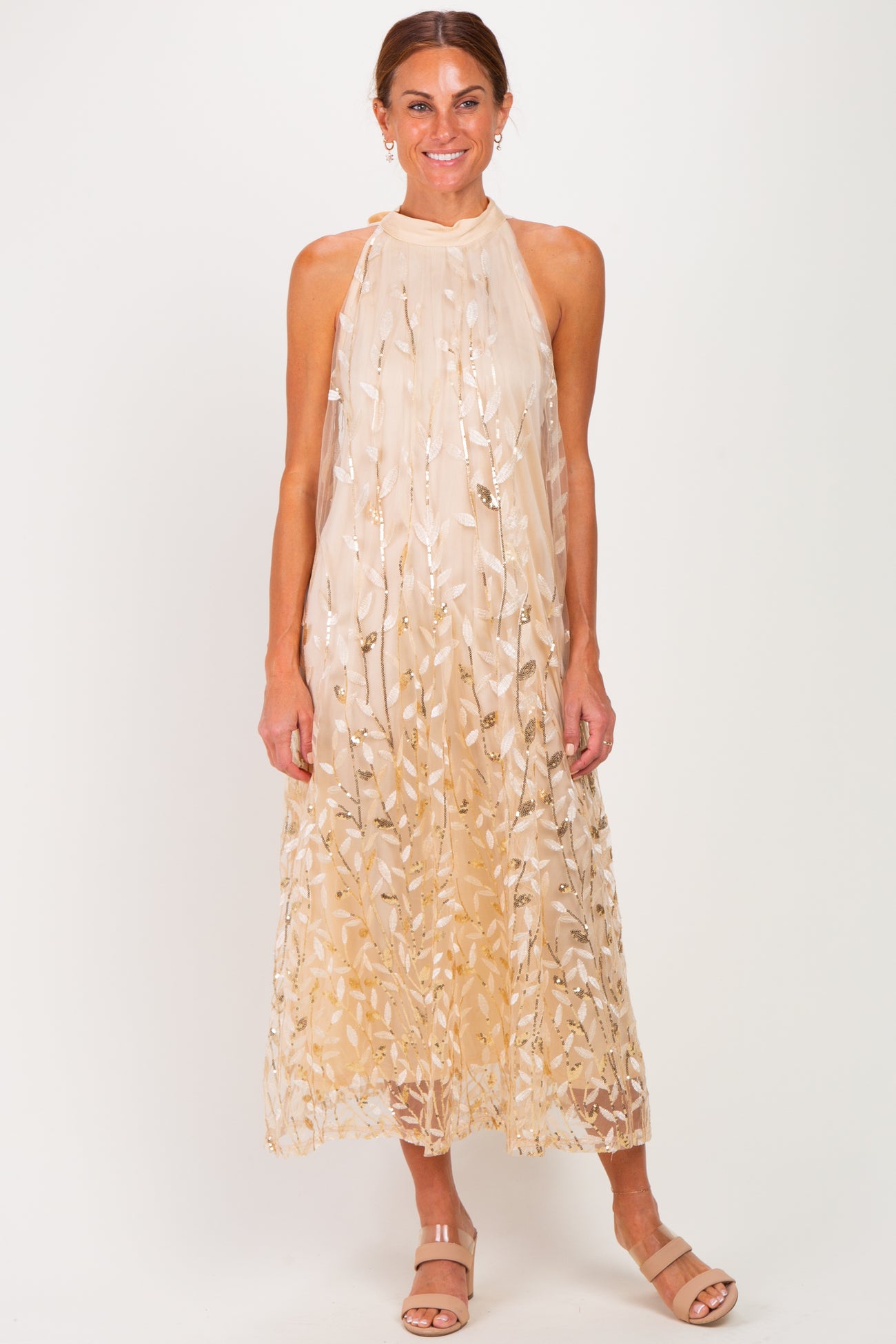 woman wearing a nude sleeveless maxi dress with gold leaf embroidery and a halter neck