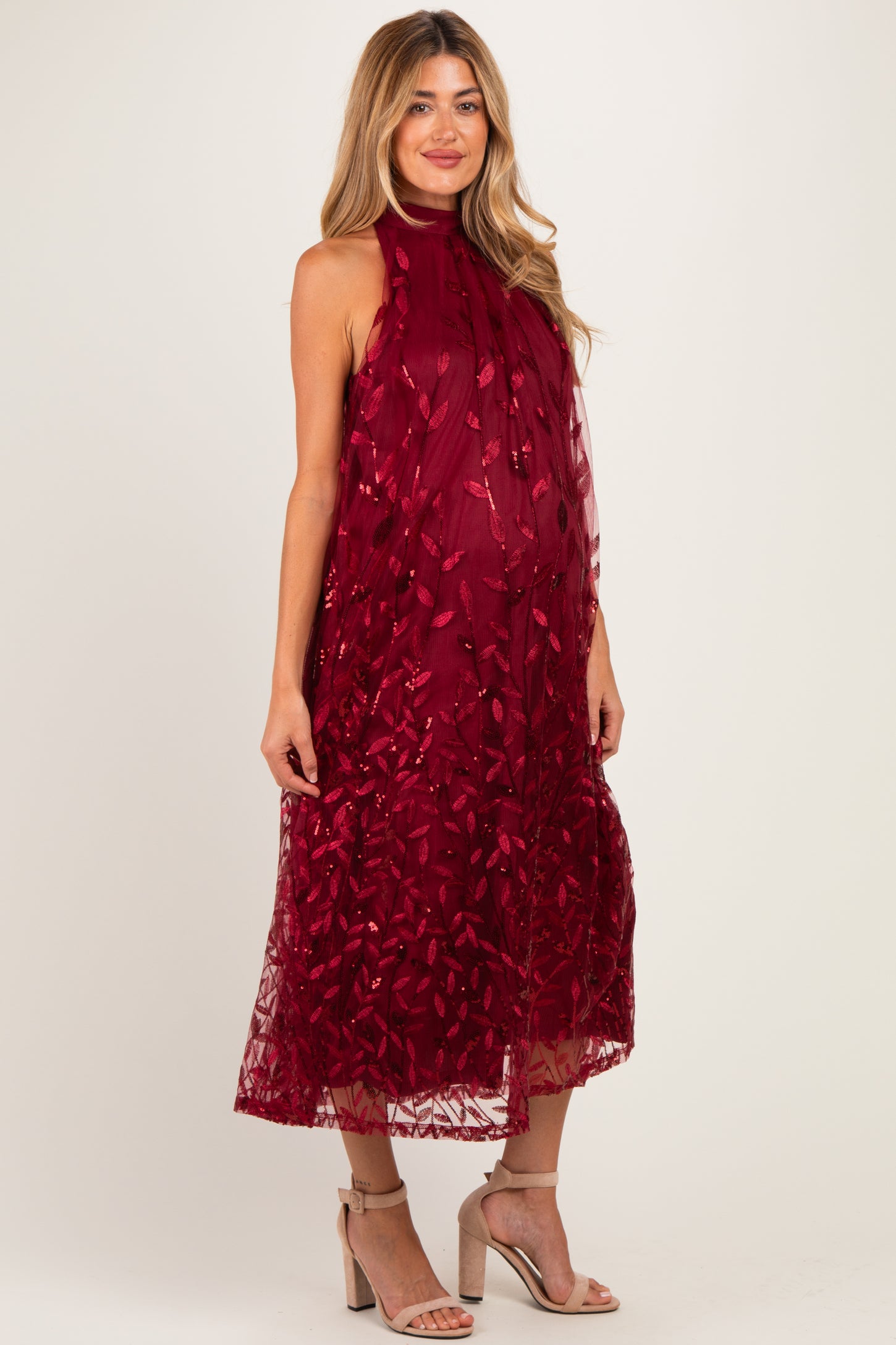 woman wearing a burgundy sleeveless maternity dress with floral embroidery and a flowing silhouette, showcasing her baby bump
